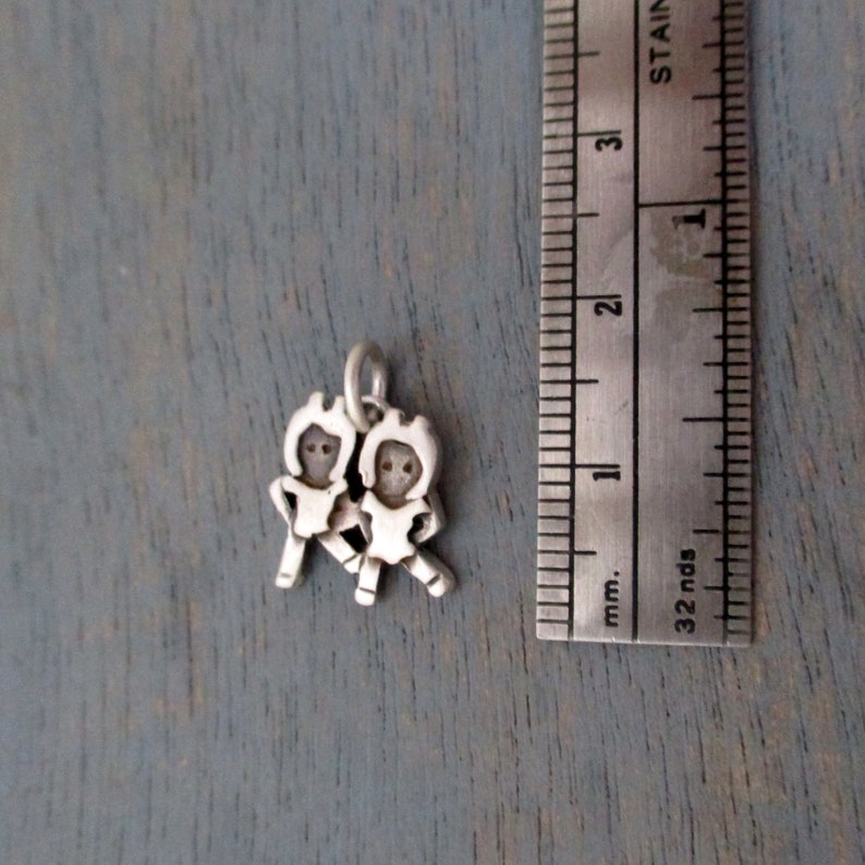 May include: Silver charm featuring two stylized figures holding hands, approximately 1 inch in size.