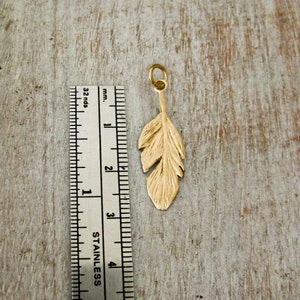 May include: A gold-colored feather charm pendant, approximately 3 cm long, is shown next to a ruler for size reference.