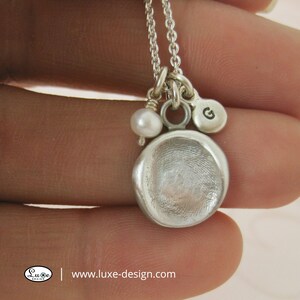 May include: Silver necklace with a fingerprint charm, a pearl bead, and a charm with the letter G. www.luxe-design.com