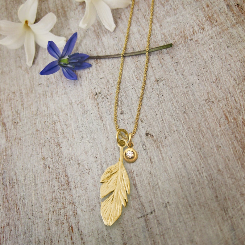 May include: A gold necklace with a delicate chain and a feather pendant. The pendant has a small diamond accent.
