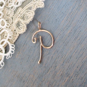 Op de afbeelding: Een gouden hanger met een cursief geschreven letter P.