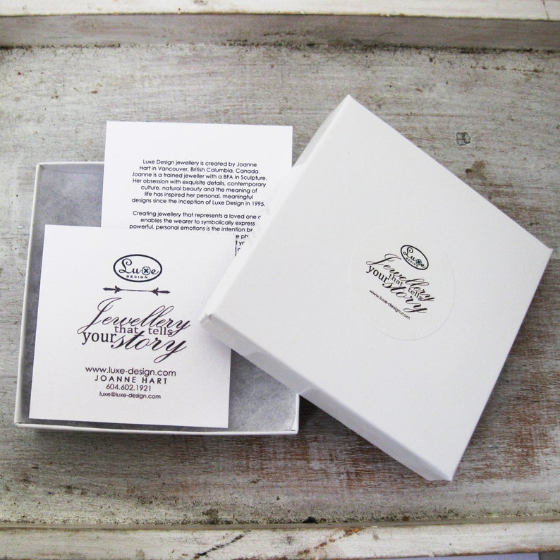 May include: White gift box with a white lid open. The box has a sticker on the lid that says "Jewellery that tells your story" and a website address. Inside the box is a white card with text about the jewelry designer.