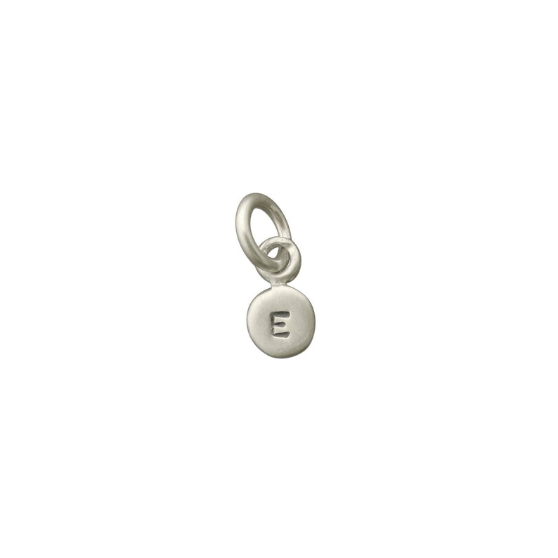May include: Silver charm with a round disc featuring the letter 'E' in a simple font. The charm has a small loop for attaching to a necklace or bracelet.