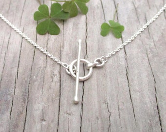 May include: A silver necklace with a toggle clasp. The clasp is a simple, round ring with a straight bar that slides through it.