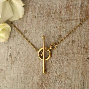 May include: A gold necklace with a toggle clasp. The clasp is a simple bar with a ring on each end. The necklace is made of a thin chain.