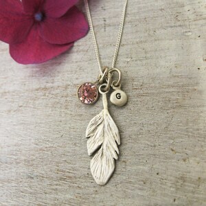 May include: A silver necklace with a feather charm, a pink crystal charm, and a silver charm with the letter "G" on it.