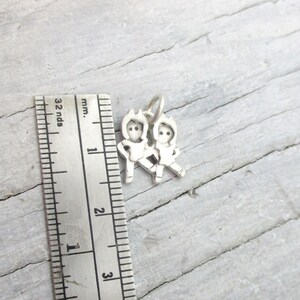 May include: Silver charm featuring two figures holding hands, approximately 1 inch in size.