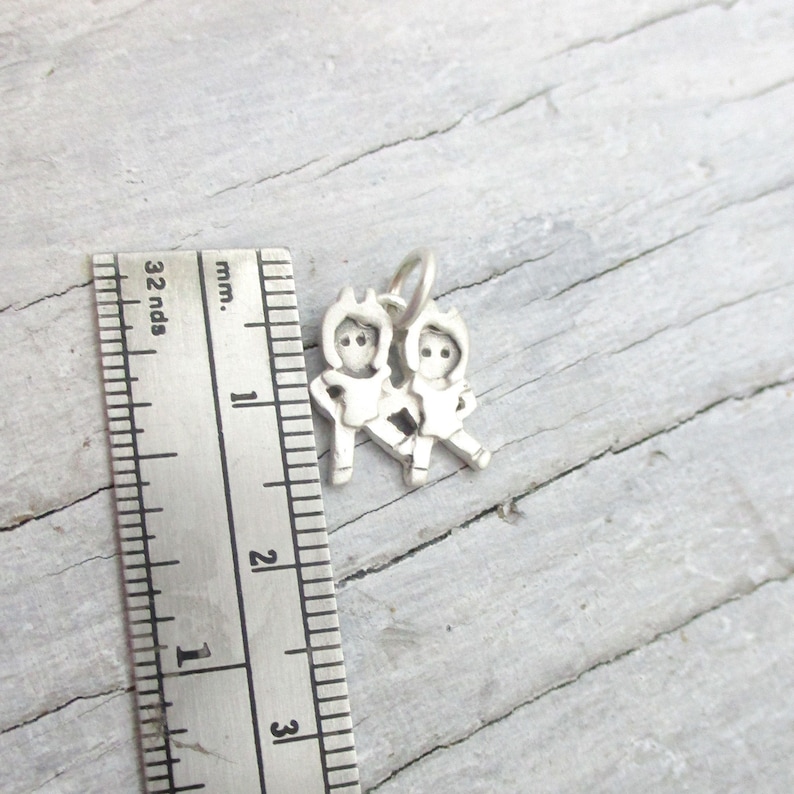 May include: Silver charm featuring two figures holding hands, approximately 1 inch in size.