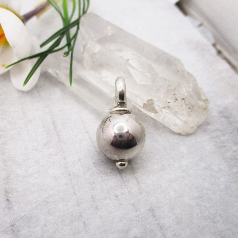 May include: A silver charm in the shape of a sphere with a small loop at the top.