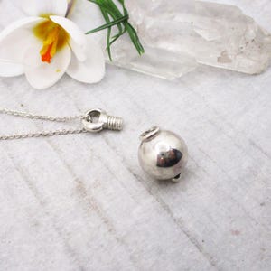 May include: A silver necklace with a round, silver pendant. The pendant is attached to the chain with a small, silver loop.