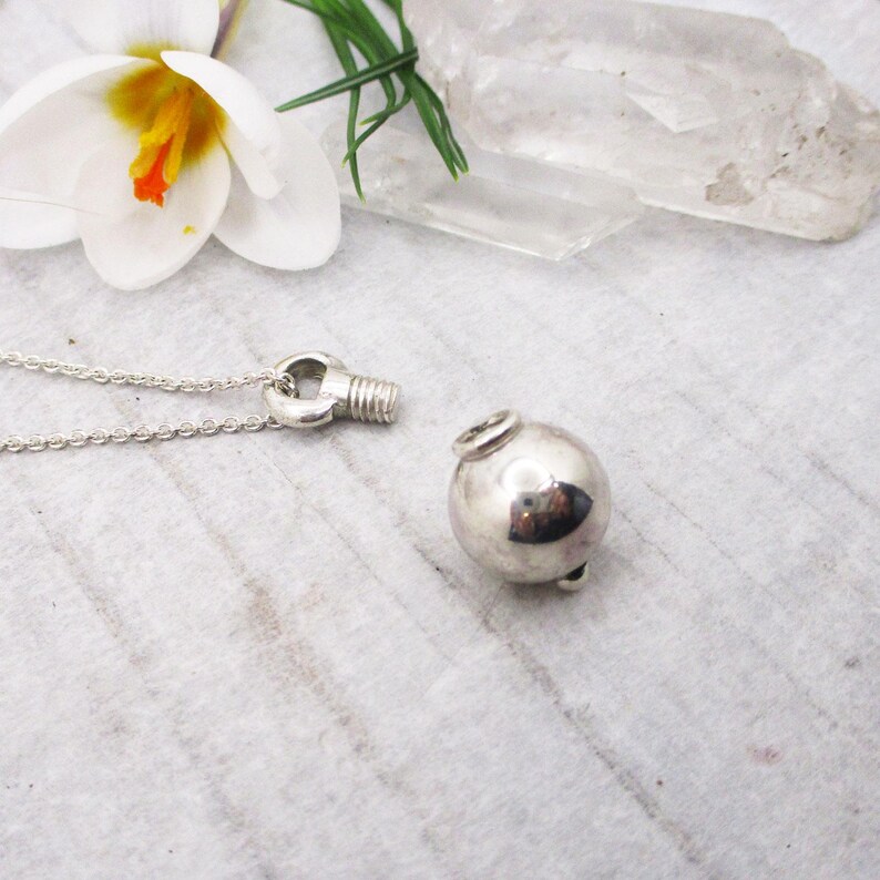 May include: A silver necklace with a round, silver pendant. The pendant is attached to the chain with a small, silver loop.