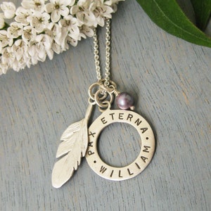 May include: Silver necklace with a feather charm, a circle charm with the words "Pax Eterna William" engraved on it, and a small purple pearl.