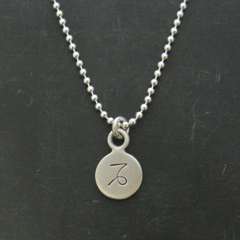 Puede incluir: Un collar de plata con un colgante redondo que presenta el s&iacute;mbolo del zod&iacute;aco de Capricornio.