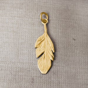 May include: A gold-colored feather charm pendant with a loop at the top for attaching to a necklace or bracelet.