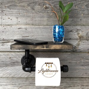Puede incluir: Un soporte para papel higi&eacute;nico de pared hecho de tuber&iacute;a industrial negra con un estante de madera te&ntilde;ida oscura encima. Un rollo de papel higi&eacute;nico blanco con el texto Lightrooom SHOP impreso est&aacute; en el tubo. Un jarr&oacute;n de vidrio con piedras azules est&aacute; en el estante.