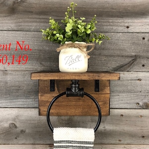 May include: A wall-mounted towel ring featuring a dark brown wooden shelf and a black metal pipe fixture. A white Ball mason jar with green foliage sits on the shelf. A white and gray striped towel hangs from the ring. Text reads Patent No. D850,149.