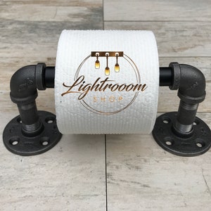 May include: Industrial-style toilet paper holder made from black metal pipes and fittings. The holder features a roll of white toilet paper and is mounted on a wooden surface. The text "Lightroom Shop" is printed on the toilet paper.