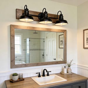 May include: A rustic bathroom vanity with a large rectangular mirror framed in light brown wood. Above the mirror, three black metal light fixtures are mounted on a dark brown wooden board. The vanity has a white sink and black faucet.