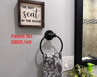 May include: A black metal towel ring with a gray and white floral patterned towel hanging from it. Above the towel ring is a framed sign that reads "THE BEST seat IN THE HOUSE". The patent number D850,149 is visible.