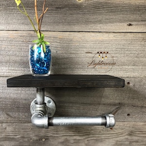 Puede incluir: Un estante de pared con una tabla de madera te&ntilde;ida de oscuro, sostenida por un soporte de tuber&iacute;a de metal industrial de tono plateado. Un florero de vidrio transparente con cuentas azules y una peque&ntilde;a planta verde descansa sobre &eacute;l.