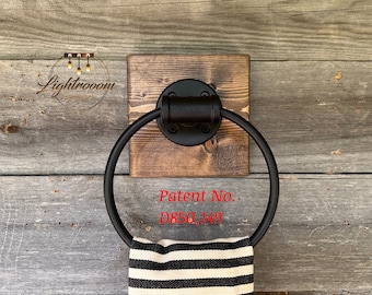 May include: A circular black metal towel ring mounted on a square dark stained wooden block. The hardware features a matte finish. A white and black striped towel hangs from the ring. The text Patent No. D850,149 is visible on the image.
