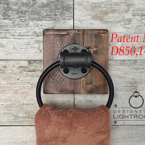 May include: A wall-mounted towel ring featuring a circular black metal hoop attached to a square, dark-stained wooden base with a black industrial pipe fitting. The text Patent No. D850,149 and DESIGNED BY LIGHTROOOM are visible on the image.