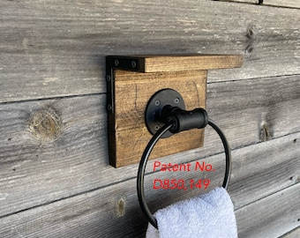 May include: A wall-mounted towel ring featuring a square stained wood backplate with a small top shelf, attached with black metal corner brackets. A black circular metal ring is secured to the wood with a round flange. Text reads Patent No. D850,149.