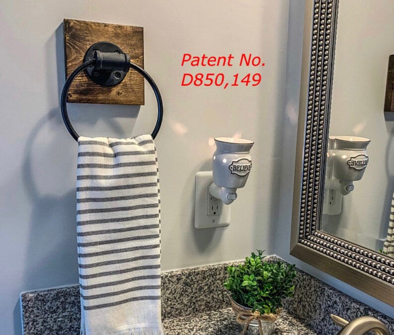 May include: A wall-mounted towel ring featuring a black metal circular holder attached to a square dark wood base. A white and gray striped hand towel hangs from the ring. The text Patent No. D850,149 is visible on the wall near the towel ring.