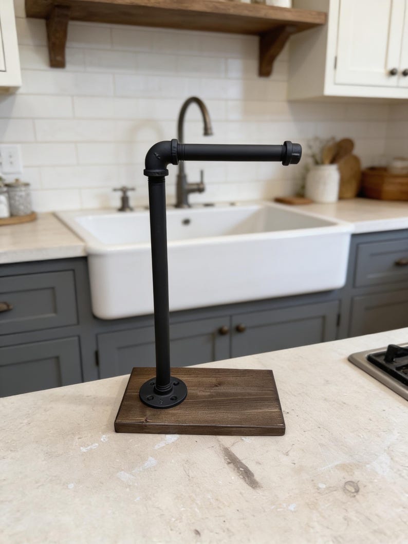 May include: A paper towel holder featuring a matte black metal pipe assembly attached to a rectangular dark brown wooden base. The vertical pipe connects to a horizontal arm via an elbow fitting, creating an L-shaped structure for holding rolls.