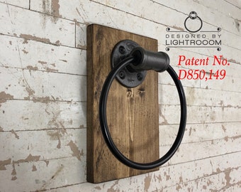 May include: A wall-mounted towel ring featuring a circular black metal ring attached to a dark brown rectangular wooden base with a black pipe flange. The text DESIGNED BY LIGHTROOOM and Patent No. D850,149 is printed in black and red on the wall.