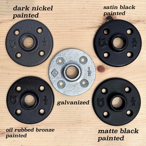 May include: A collection of pipe flanges in various finishes: dark nickel, satin black, galvanized, oil rubbed bronze, and matte black. Each flange has a central hole and four smaller holes for mounting, with "1/2" markings.