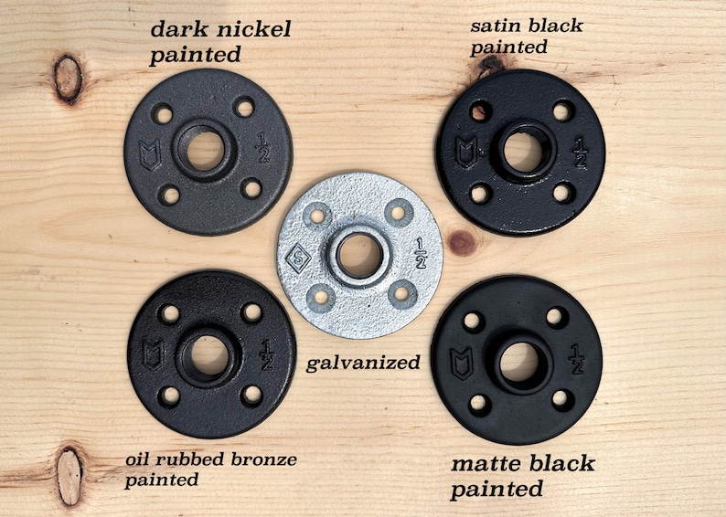 May include: A collection of pipe flanges in various finishes: dark nickel, satin black, galvanized, oil rubbed bronze, and matte black. Each flange has a central hole and four smaller holes for mounting, with "1/2" markings.