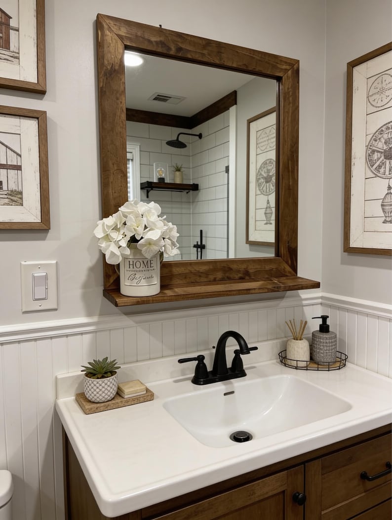 May include: A bathroom vanity with a white sink, black faucet, and a large wooden-framed mirror. The mirror reflects a shower and decorative items. A white ceramic pot with the word "HOME" and white flowers sits on a shelf below the mirror.