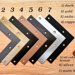 May include: A selection of seven L-shaped metal brackets in different finishes: dark nickel, gold, satin black, copper, oil-rubbed bronze, silver, and matte black. Each bracket has pre-drilled holes for mounting.