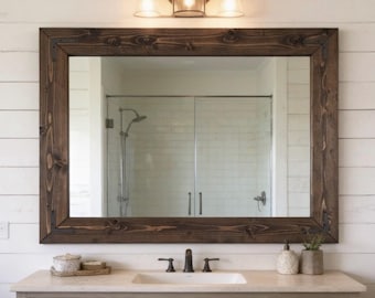 May include: A rectangular wall mirror featuring a dark brown stained wood frame with visible wood grain and knots. The frame is accented with dark metal corner brackets. The mirror reflects a bathroom interior with a shower and a vanity light fixture.