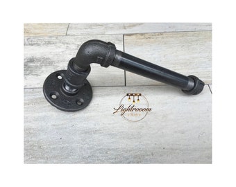May include: Black industrial pipe towel bar. The bar features a round flange with four holes for mounting, a 90-degree elbow, and a straight pipe section. The metal has a matte finish, suitable for a rustic or modern bathroom.
