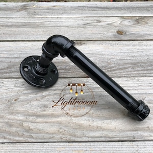 May include: Black industrial pipe towel rack with a round flange base and a 90-degree elbow. The rack is made of black metal and has a threaded end. The image includes the text "Lightroom Shop".