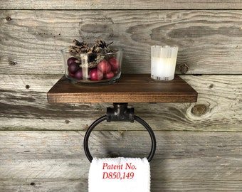 May include: A dark brown wooden shelf with a black metal pipe towel ring attached underneath. A clear glass bowl filled with pinecones and red berries sits on the shelf next to a white candle. A white towel hangs from the ring with Patent No. D850,149.
