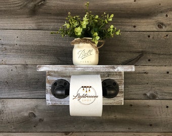 May include: A wall-mounted toilet roll holder featuring a white distressed wooden shelf, black industrial pipe fittings, and a roll of white toilet paper with a circular logo that reads Lightrooom SHOP. A white Ball mason jar with greenery sits on top.