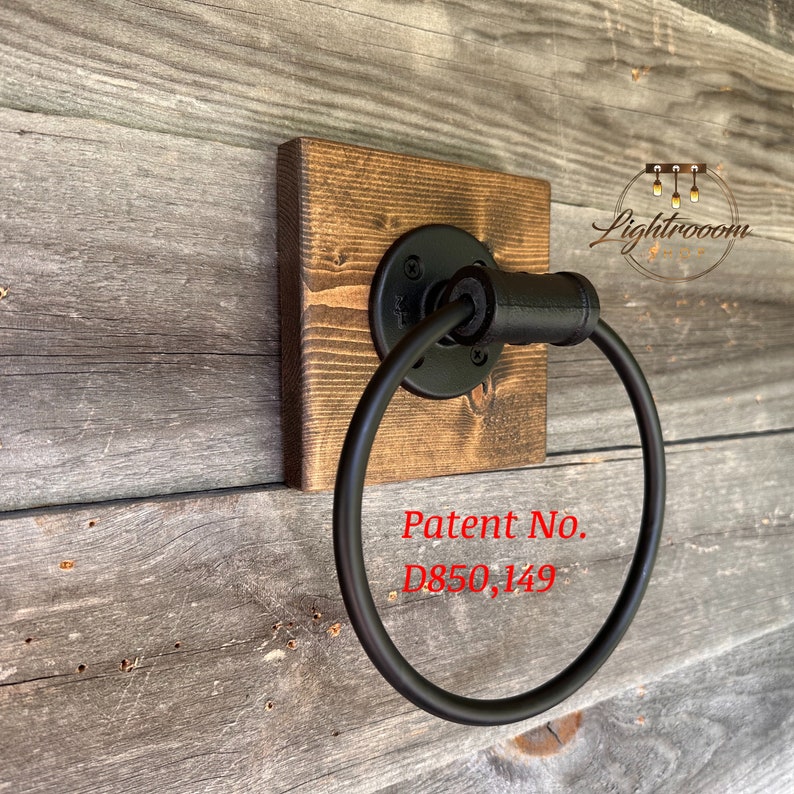 May include: A wall-mounted towel ring featuring a circular black metal ring attached to a square dark brown stained wooden base. The hardware includes a black metal pipe flange and connector. The text Patent No. D850,149 is visible on the image.