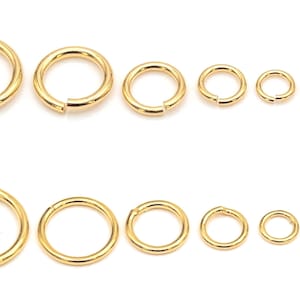 May include: A collection of gold-colored jump rings in various sizes, arranged in two rows. The rings are round and have a small opening for attaching to other jewelry components. The sizes range from large to small.