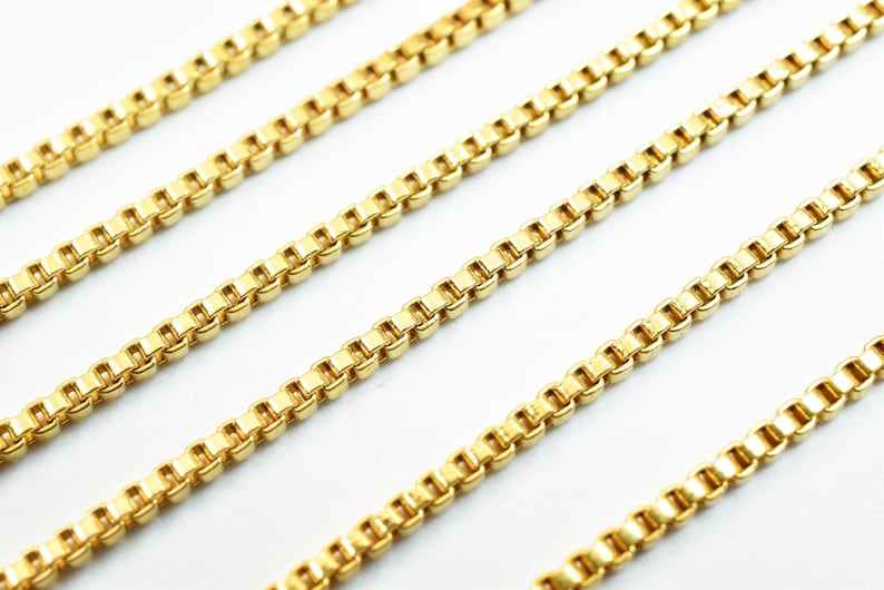 Puede incluir: Cuatro hebras de cadena de oro, cada una con un patr&oacute;n de cadena de caja, se colocan sobre una superficie blanca.