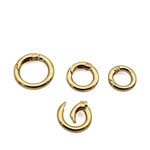 May include: Four gold-colored spring ring clasps in varying sizes. Three are circular, and one is a spiral shape. The clasps have a shiny, metallic finish and are designed for jewelry making or crafts.
