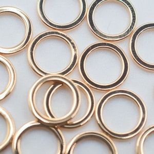 May include: A collection of multiple circular gold-toned metal rings scattered across the frame. Each ring features a smooth, polished surface with a consistent thickness and a reflective finish, creating a uniform appearance throughout the group.