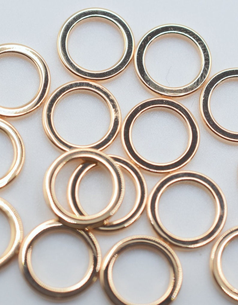 May include: A collection of multiple circular gold-toned metal rings scattered across the frame. Each ring features a smooth, polished surface with a consistent thickness and a reflective finish, creating a uniform appearance throughout the group.