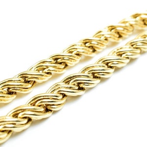 May include: A close-up of a gold rope chain necklace. The chain is made of thick, interwoven links, creating a textured and luxurious look.