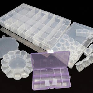 Puede incluir: Una colección de contenedores de almacenamiento de plástico transparente con varias configuraciones de compartimentos. Incluye cajas rectangulares, una caja morada y un recipiente con borde festoneado. También hay una regla de metal.