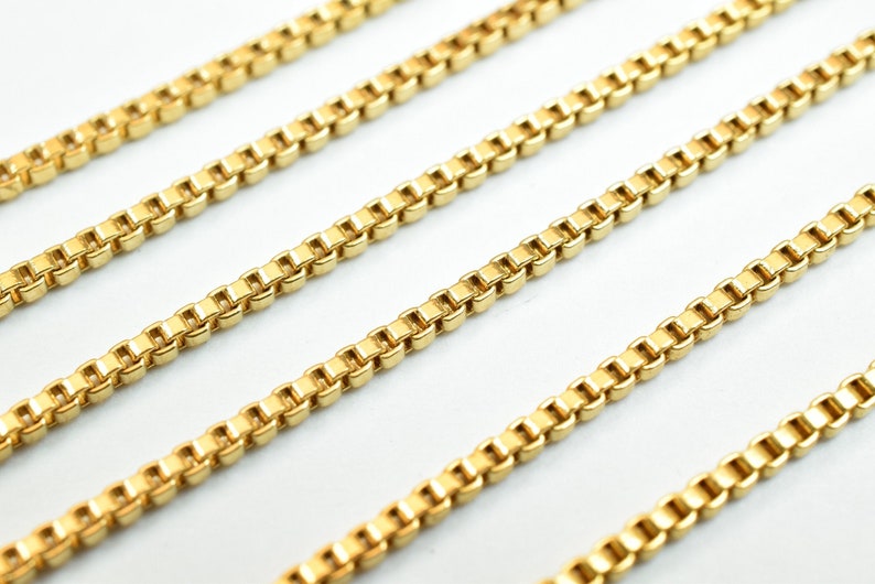 Puede incluir: Cuatro hebras de collar de cadena de eslabones de oro, dispuestas en l&iacute;neas paralelas sobre una superficie blanca.