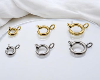以下が含まれることがあります： 2列に並べられた6つの円形スプリングリングクラスプ。上段にはサイズの異なる3つのゴールドトーンの金属製クラスプがあり、下段にはそれに対応するサイズの3つのシルバートーンの金属製クラスプが配置されています。各クラスプには小さなループが付いています。