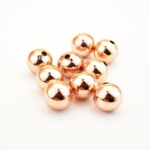 Peut inclure: Un groupe de dix perles en m&eacute;tal de couleur or rose. Les perles sont rondes et ont une finition lisse et brillante.